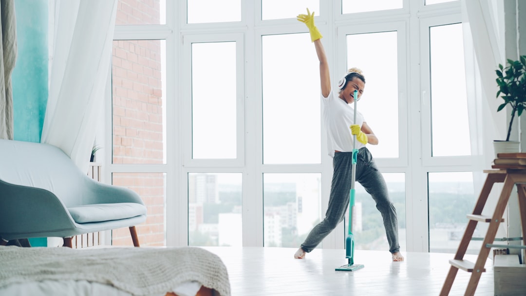 Joyful young woman is enjoying music in headphones, dancing and singing during routine cleanup at home, girl is mopping floor and having fun. People, technology and houses concept.